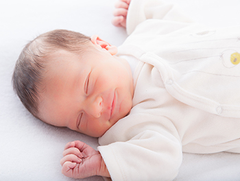 Smiling baby in fuzzy pajamas sleeping on their back.