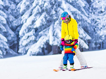 Parent helping young child learn to ski on nice winter day.