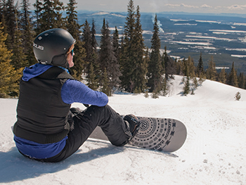 Snowboarder taking a break sitting on the snow looking at the view from Murray Ridge in Fort St. James, BC.