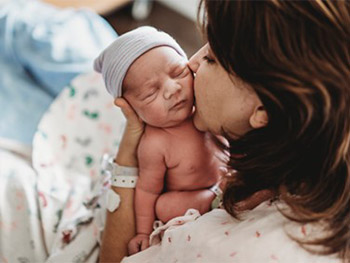 Woman holding and kissing infant on the cheek.