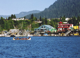 Traditional manned canoe on a bay with marina building in background.